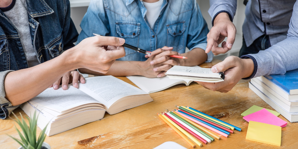 A small group of students working together with a tutor in a focused session, notebooks open