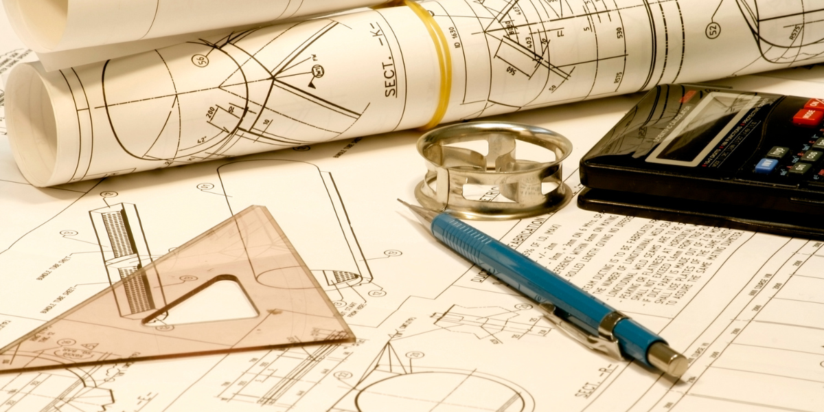 A student working on an engineering project with technical drawings and a laptop on their desk